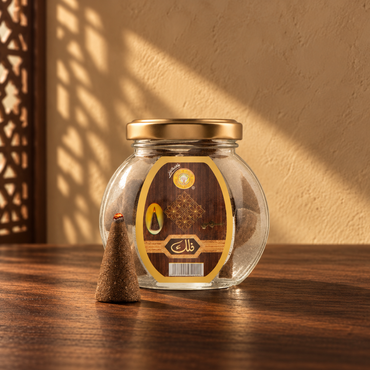 Falak Pyramid Maamoul 50 g from Sedr Al-Khaleej; round glass incense jar with a brown label, gold lid and one cone on walnut wood in angled sunlight.
