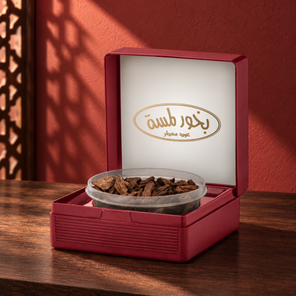 Lamsa Bakhoor Scented Oud 50 g from Sedr Al-Khaleej; open burgundy presentation case with its tub of agarwood chips on walnut wood against a brick red wall, with angled sunlight and a wooden screen shadow.
