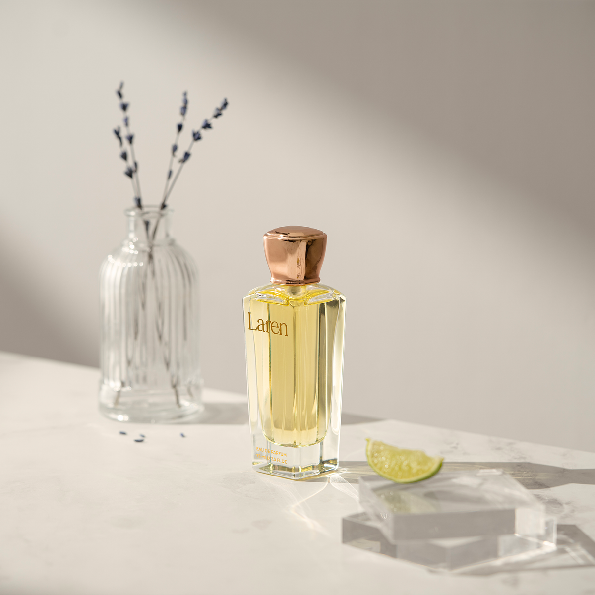Laren Perfume on marble beside a glass vase of lavender and a lime slice on a clear block