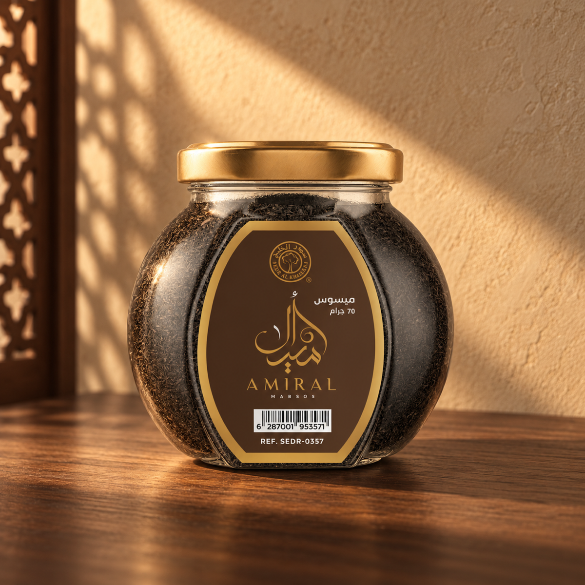 Amiral Mabsos 70 g from Sedr Al-Khaleej; closed glass jar with a gold lid on walnut wood against a sand plaster wall, lit by angled sunlight with a wooden screen shadow on the left.