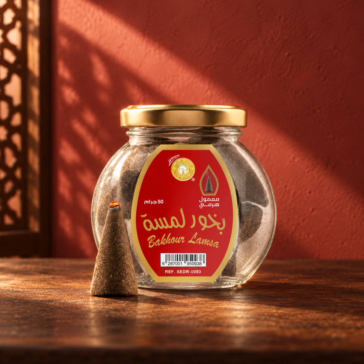 Lamsa Bakhoor Pyramid Maamoul 50 g from Sedr Al-Khaleej; round glass incense jar with a red label, gold lid and one cone on walnut wood in angled sunlight.