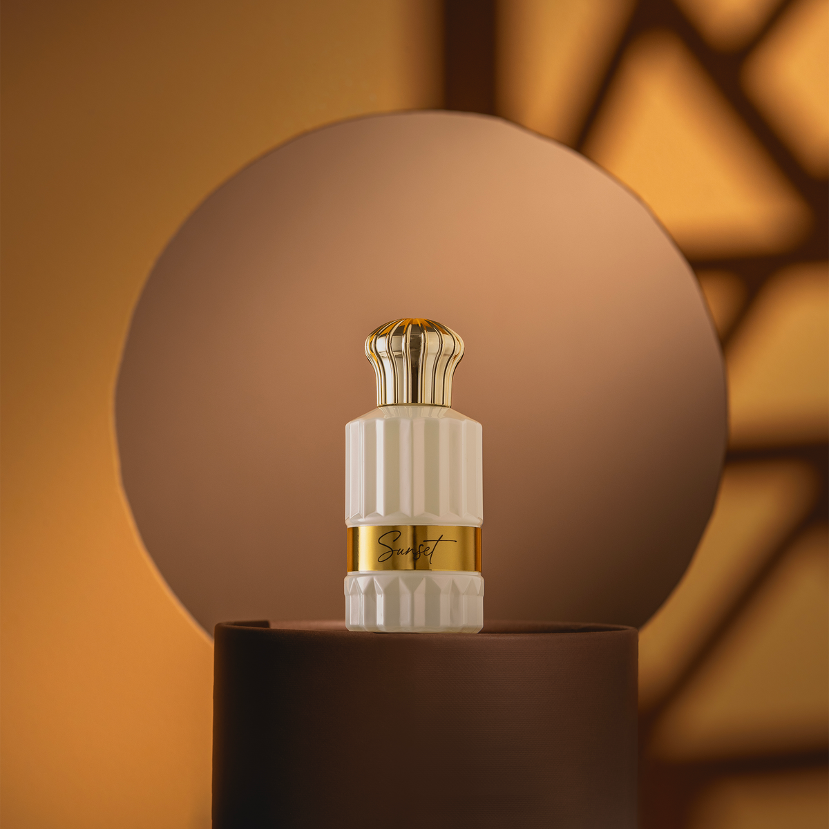 Sunset perfume bottle in front of a round disc in warm light